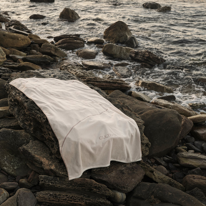 A Beach Towel in Rose lying on rocks by the sea