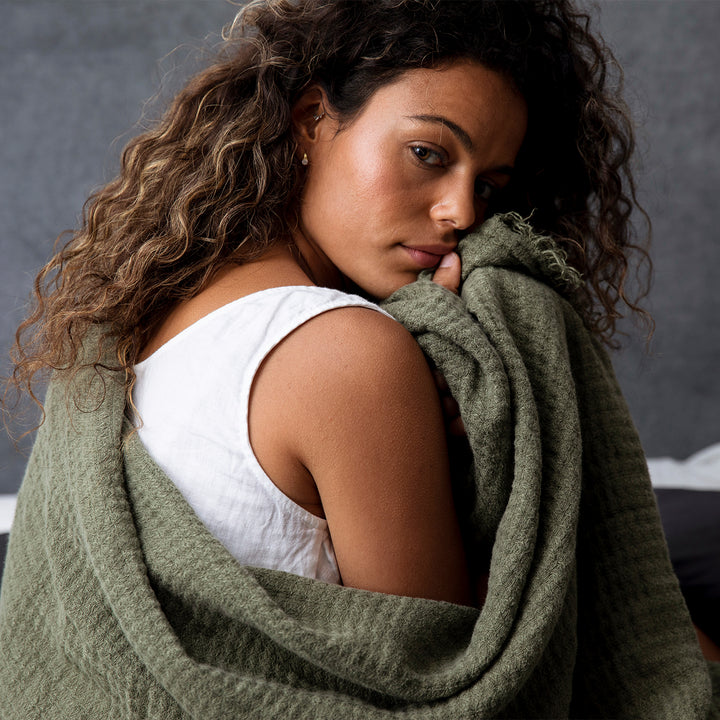  A woman with an Estela Linen Waffle Throw in Forest wrapped around herself