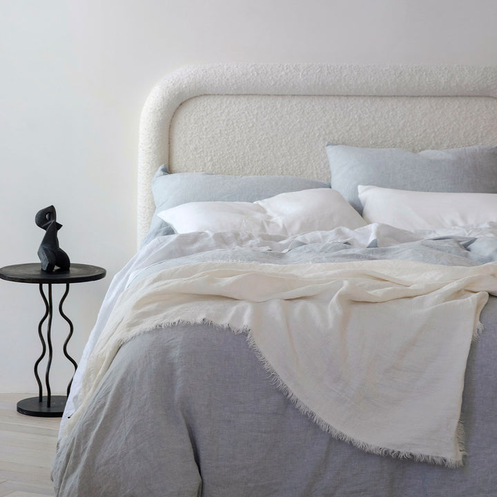 A bed dressed Sky and White bed linen, styled with a Freya Linen Throw in Snow and a black bedside table. Sizes: Queen, King