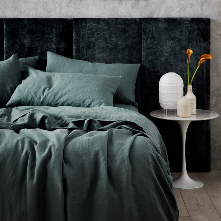 A bed dressed in Bluestone, styled with a velvet headboard, white bedside table, ceramic vases and a white lantern lamp. Sizes: Queen, King