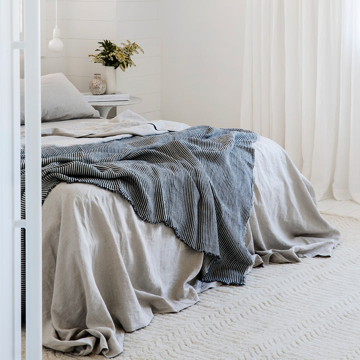 A bed dressed in Smoke Gray bed linen, styled with a Mira Linen Throw in Ellis Stripe
