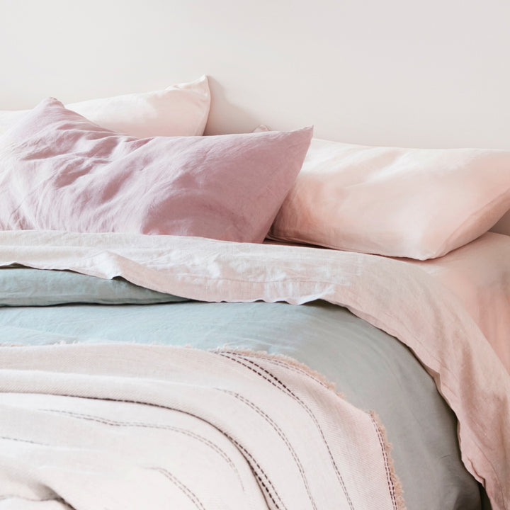 A close up of a bed dressed in Blush, Dusk, Sage and Smoke Grey bed linen, styled with a Mira Throw in Ana