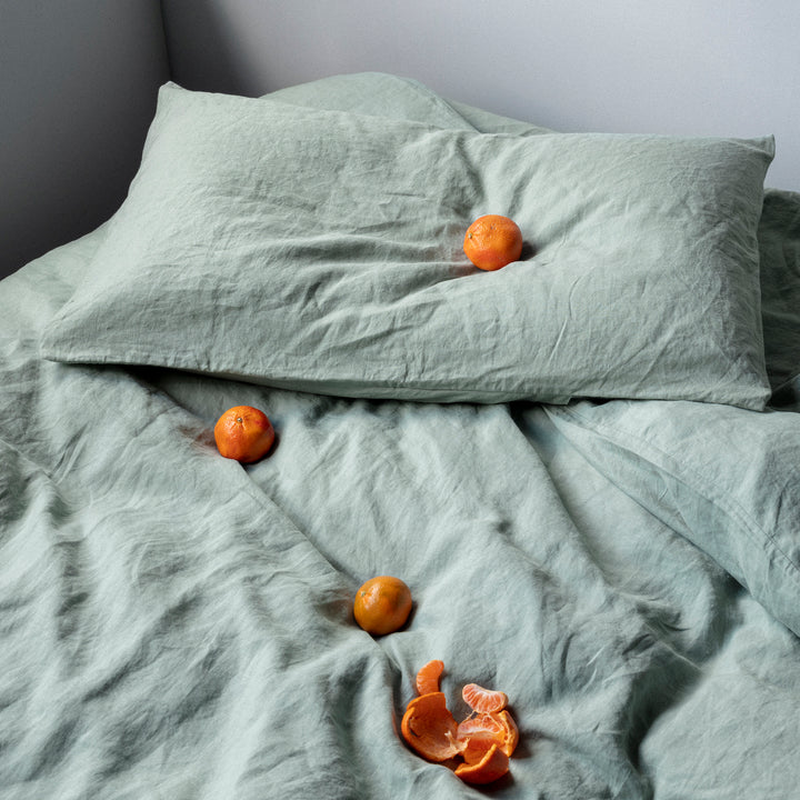 A bed dressed in Sage bed linen, styled with mandarins