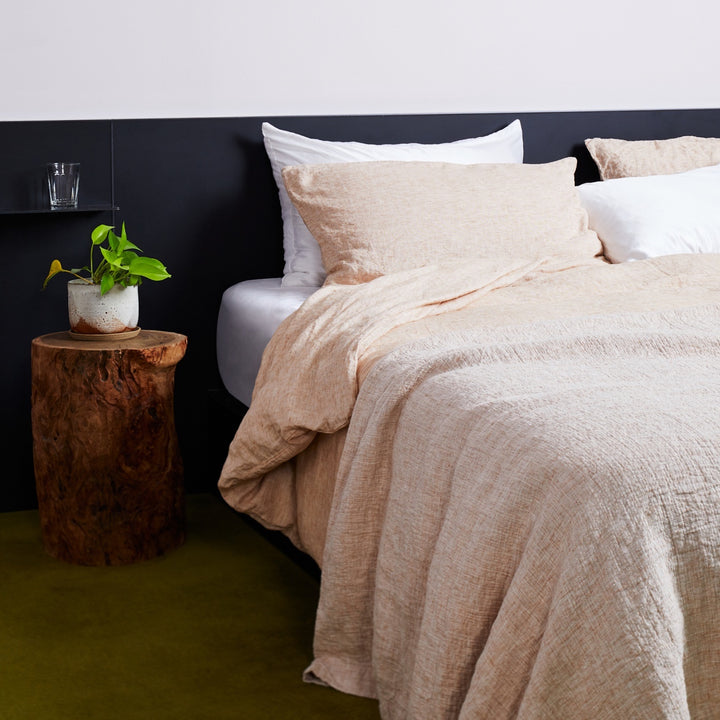 A bed dressed in Cinnamon and White bed linen, styled with a bedside table and plant