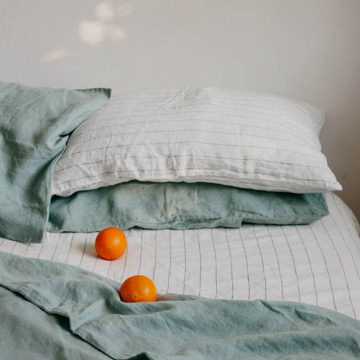 A bed dressed in Sage and Pencil Stripe bedlinen, with oranges scattered on the Duvet Cover.