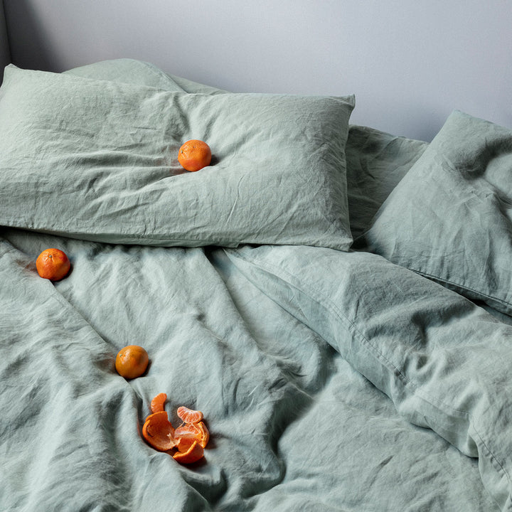 A bed dressed in Sage bed linen, styled with mandarins. Sizes: Queen, King