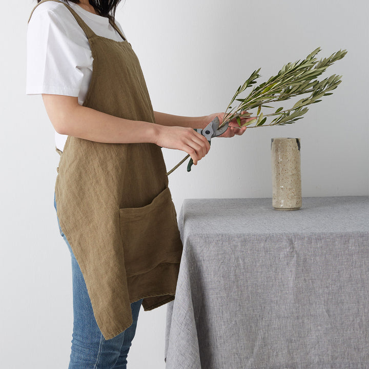 Model wearing Jude Linen Apron in Olive cutting olive branch