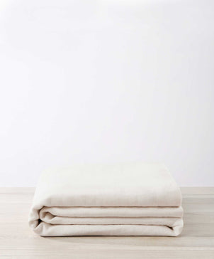 The Heavyweight Linen Bedcover - Ivory is neatly folded on a light wooden surface, set against a plain, light-colored background.
