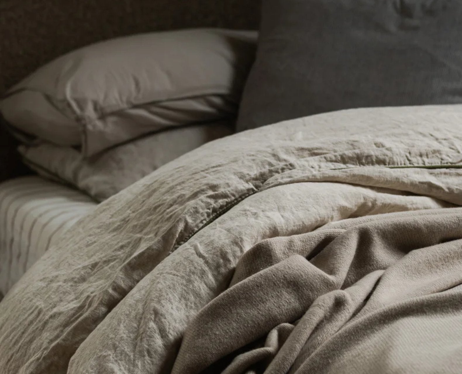 Close-up of beige bedding with pillows in a dimly lit room