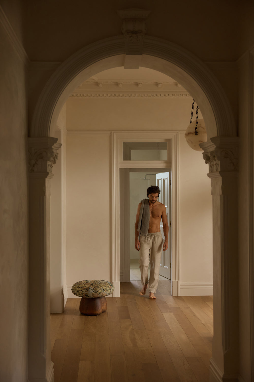 Man walking through a hallway with a decorative stool and archway.