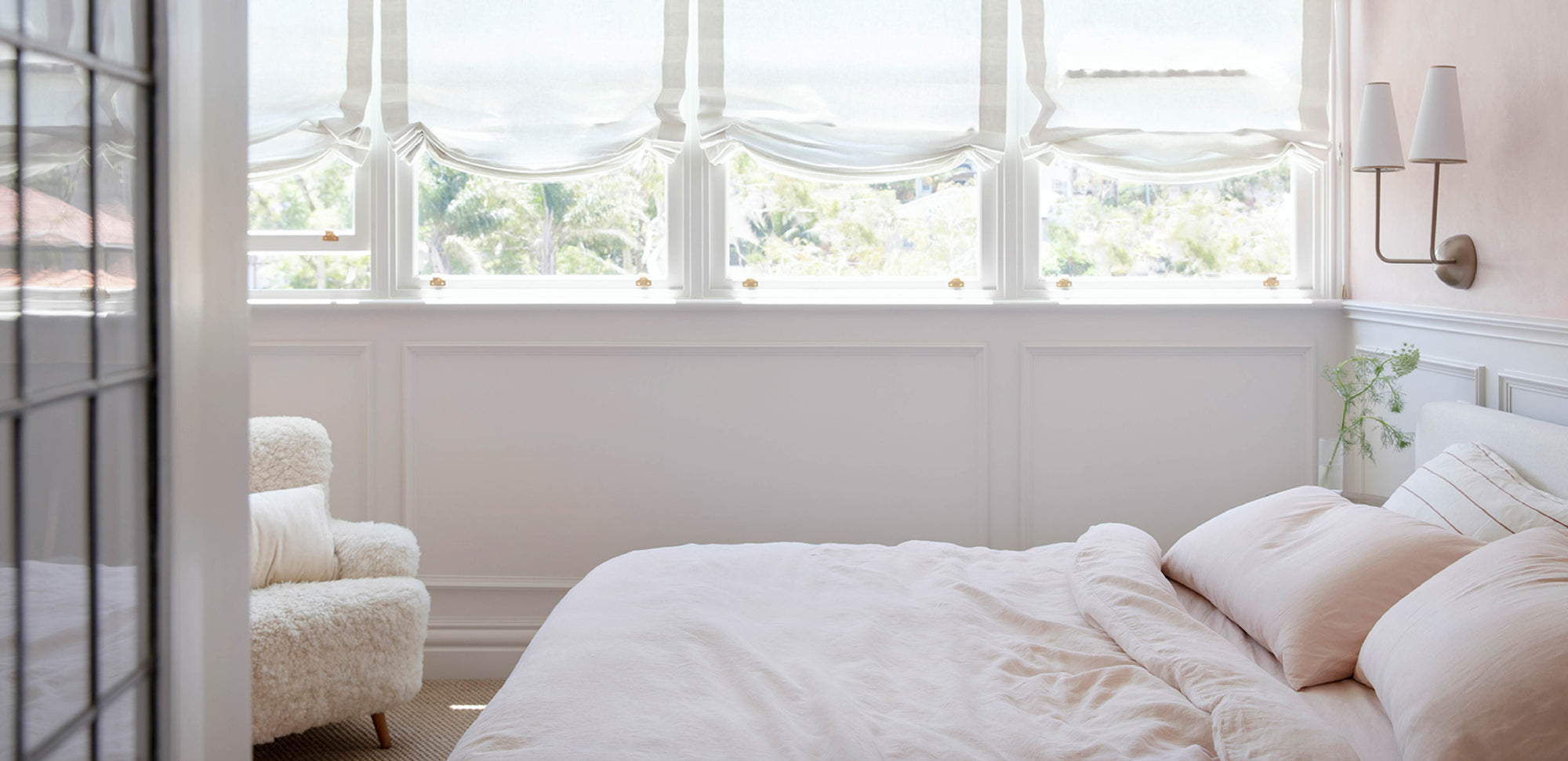 Neatly made bed in a bright bedroom with large windows.