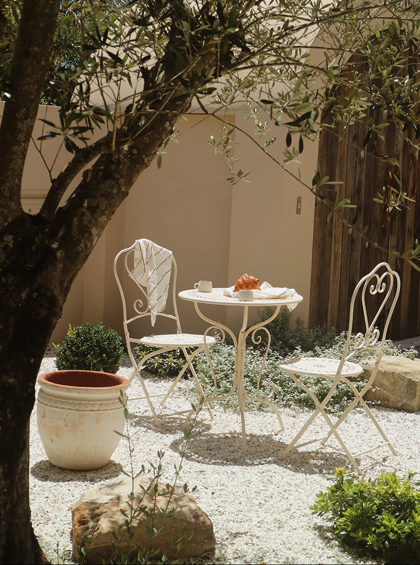 Outdoor patio setting with white table and chairs under an olive tree.