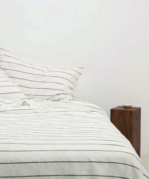 Bed with striped bedding and a wooden nightstand against a white wall