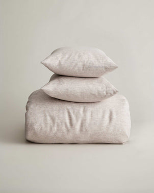 Two pillows stacked on top of a folded Rocco Duvet Cover Set - Natural in a neutral speckled fabric.