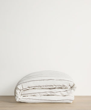 Folded beige comforter on a wooden surface with a white background