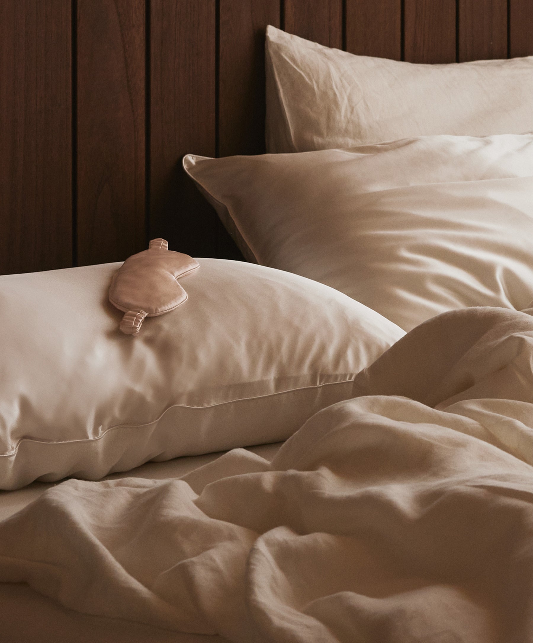 Beige pillows and bedding on a bed with a wooden headboard.