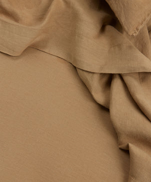 A close-up of the Linen Flat Sheet with Border in Sand, featuring smooth, light brown linen softly draped in gentle folds for a vintage look.