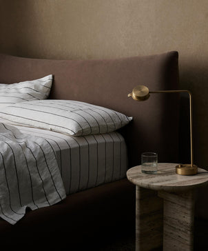 Bed with striped bedding and pillows next to a side table with a lamp and glass.