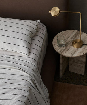 Bed with striped bedding and a gold lamp on a marble nightstand.