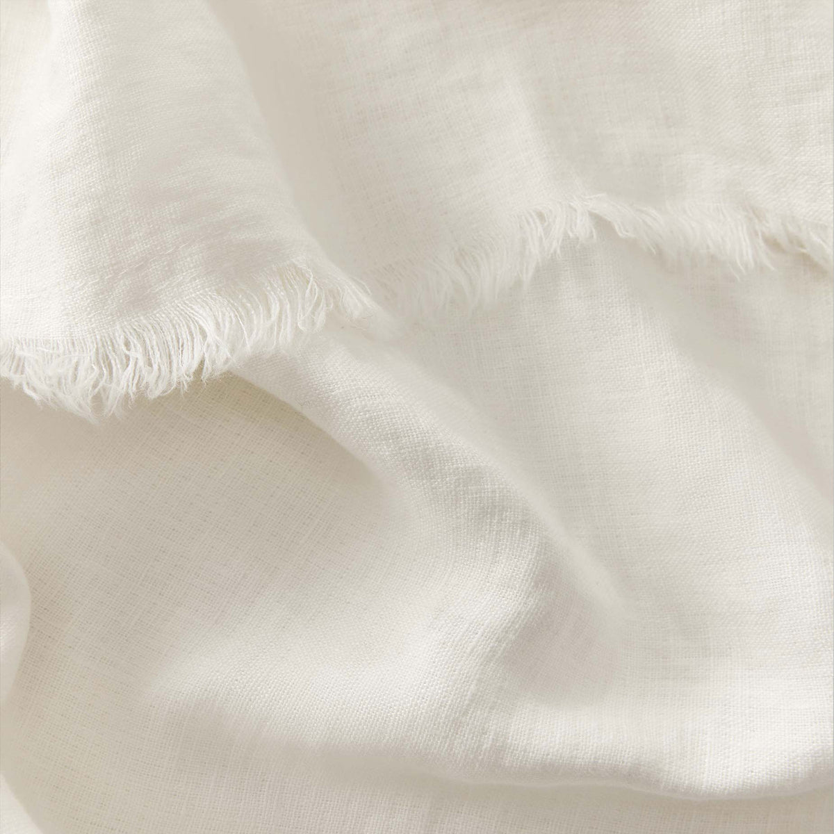 A close-up of soft, off-white fabric with a frayed edge and a subtle, woven texture, creating gentle folds and shadows.