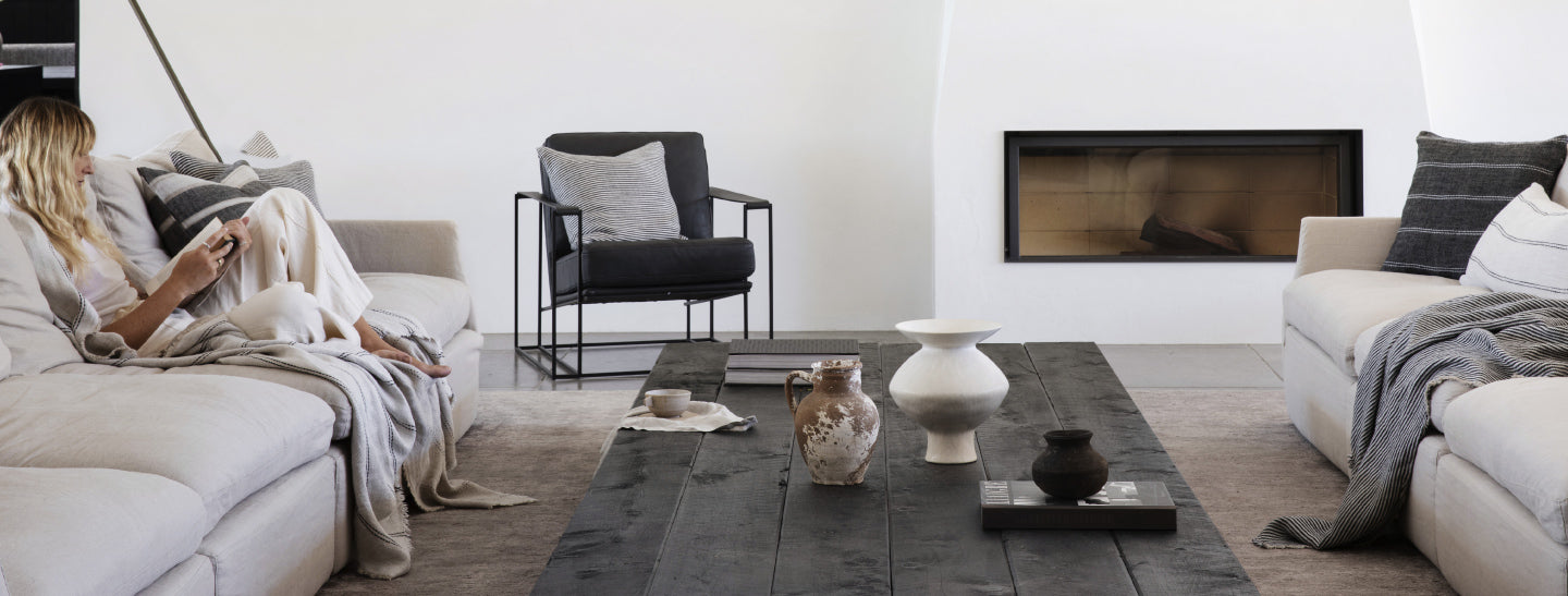 Modern living room with a woman on a sofa, coffee table with decorative items, and a fireplace.