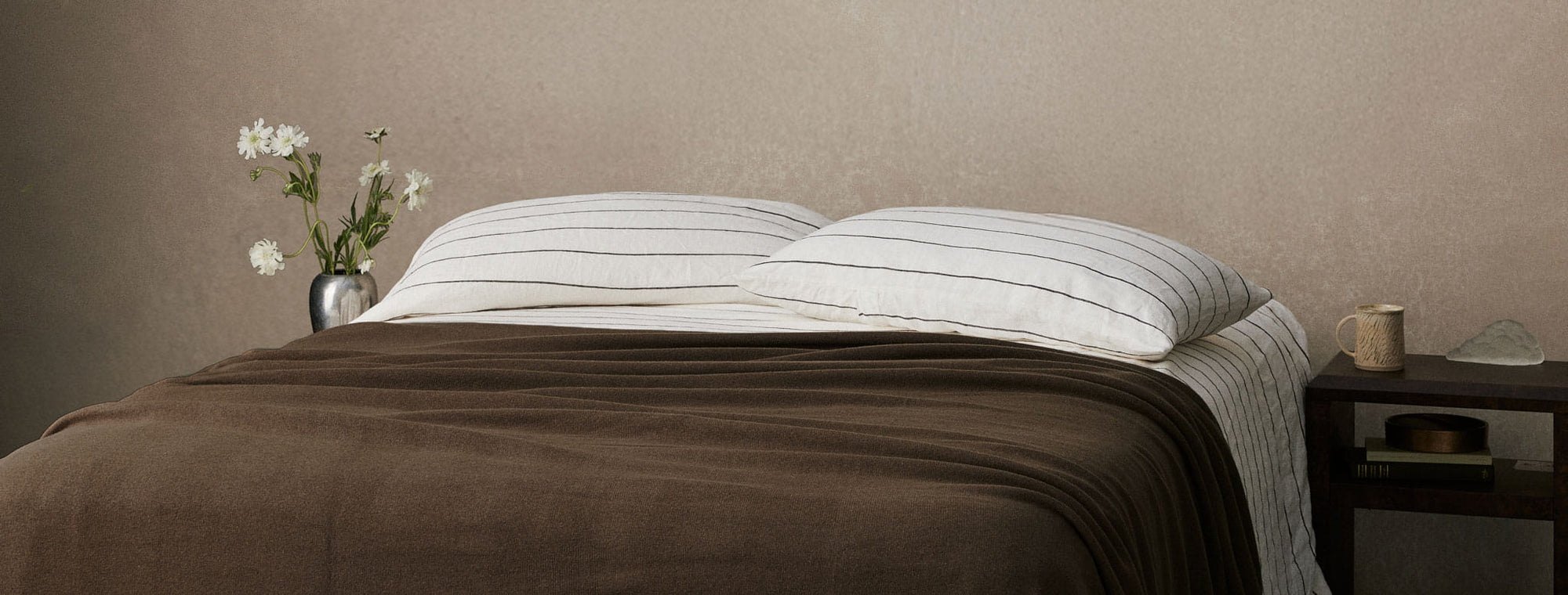 Bed with striped pillows and brown blanket against a beige wall