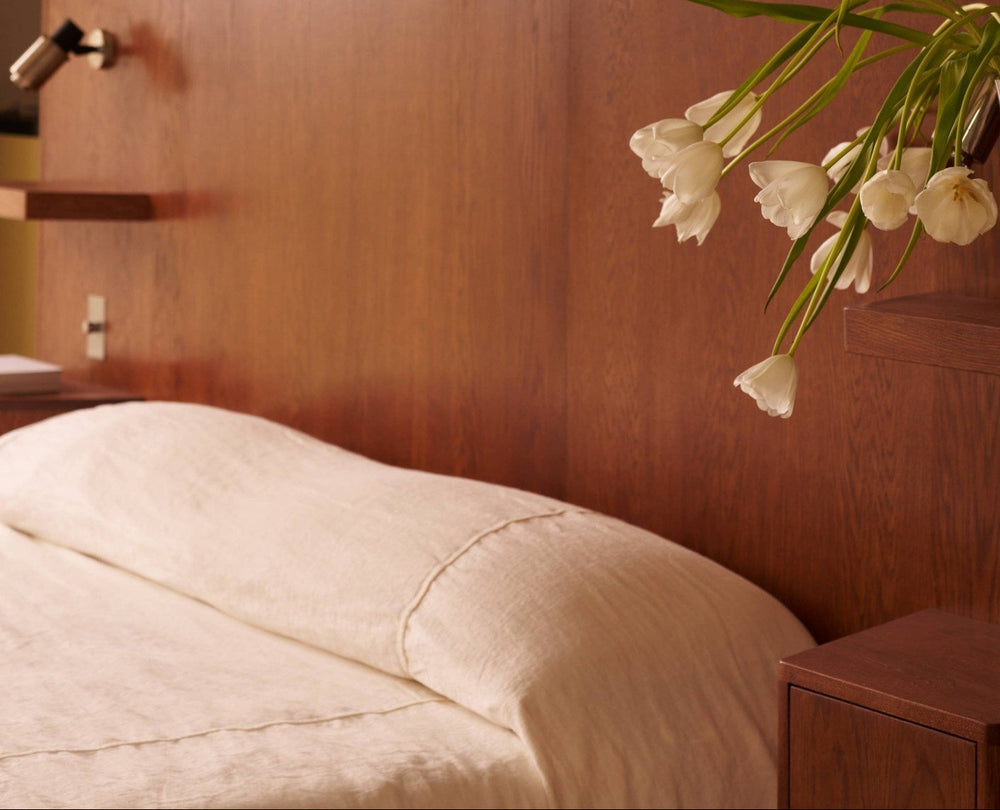 Neatly made bed with white bedding in a room with wooden walls and a vase of white tulips.