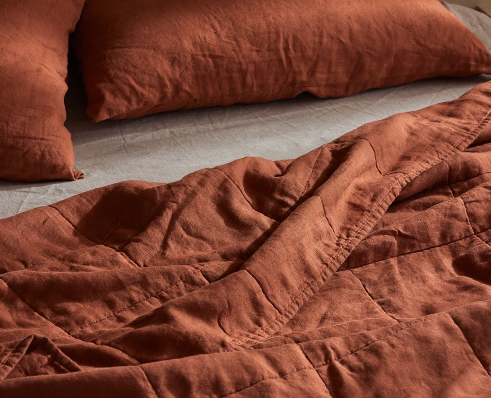 Close-up of a textured brown blanket and pillows on a bed.