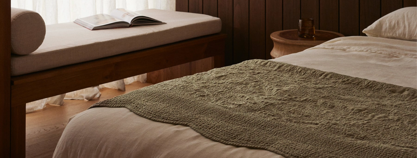 Bedroom with a bed covered in a green blanket, wooden bench, and open book.