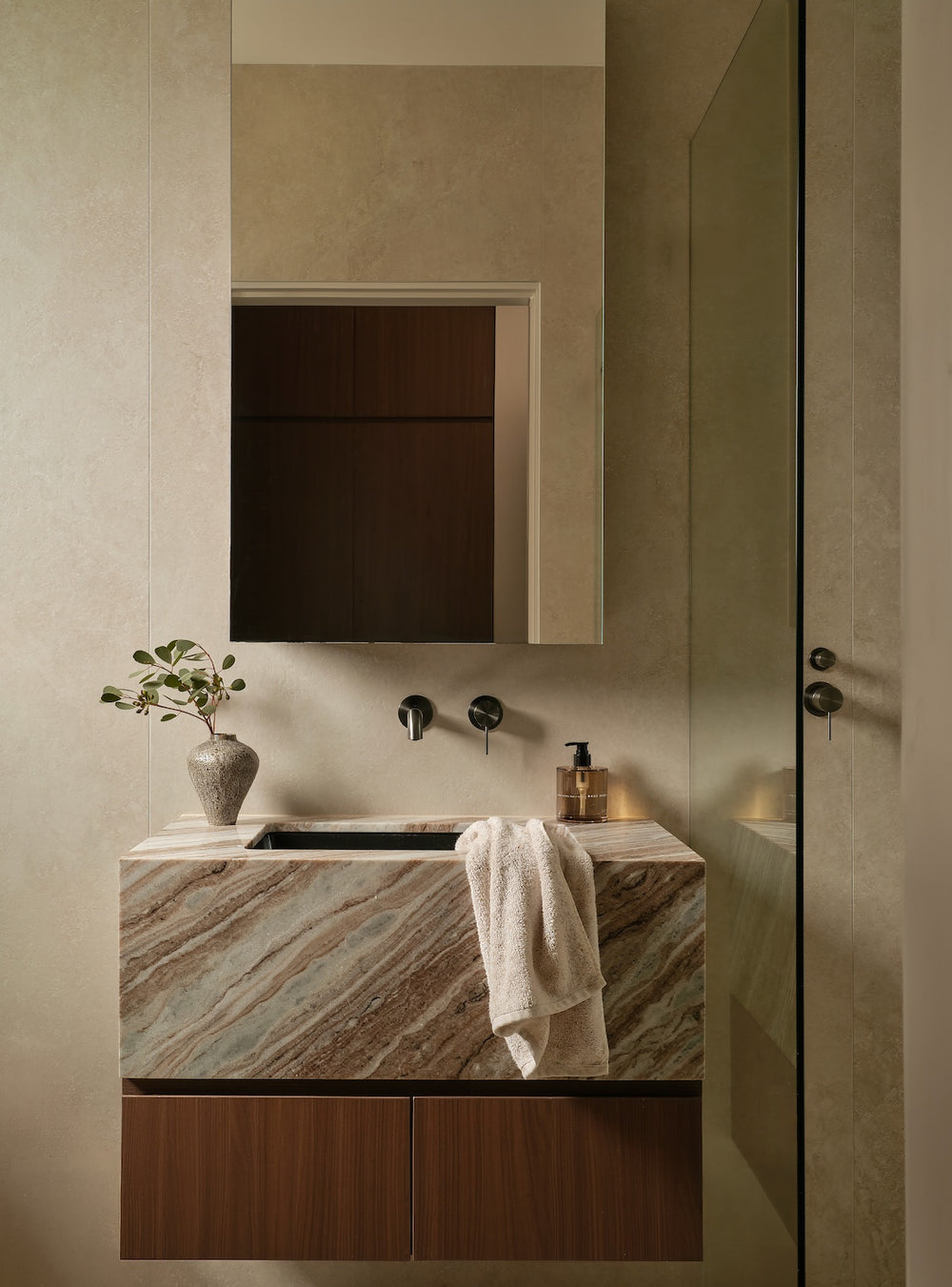 A modern bathroom vanity featuring a floating marble sink countertop with brown and beige veining, dark wood lower cabinets, a matching wall-mounted mirror, and a draped white towel.