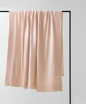 The 100% NZ Merino Wool Throw - Blush, crafted from pure New Zealand wool, hangs over a black metal bar, set against a plain white background.