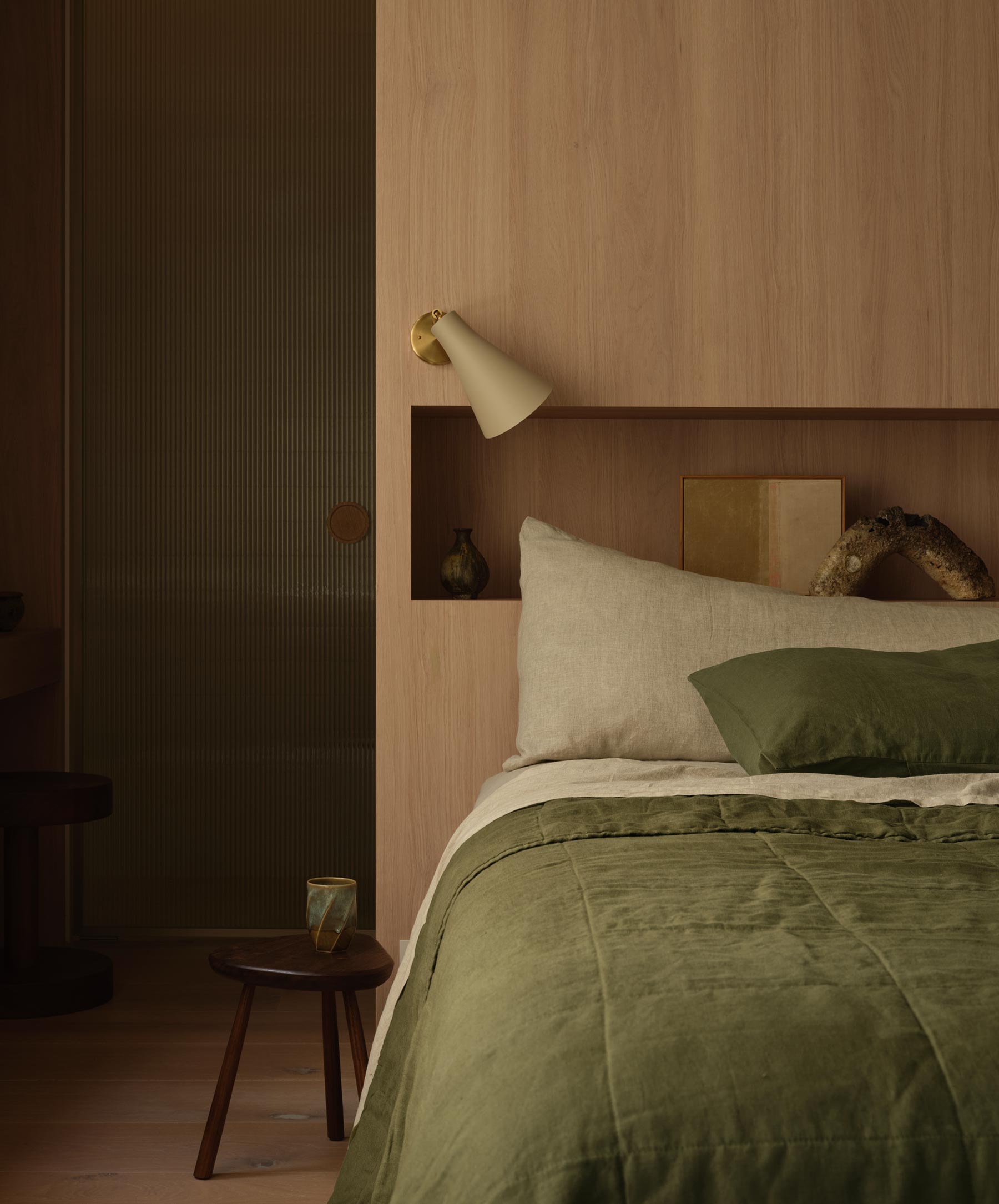 Bedroom with green bedding and wooden headboard, dimly lit.