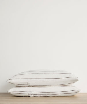Two white pillows with black stripes stacked on a wooden surface against a light gray background