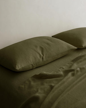 Set of 2 CULTIVER linen pillowcases in Forest color, styled on a bed, showcasing soft, natural bed linen for a cozy look.