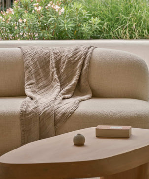 Beige sofa with a textured blanket draped over it, set against a green outdoor background.