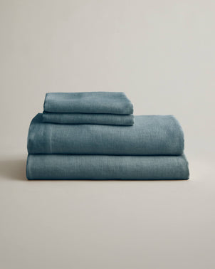 Folded blue linen sheet set with matching pillowcases by CULTIVER, showcasing soft, breathable bed linen for a relaxed bedroom look.