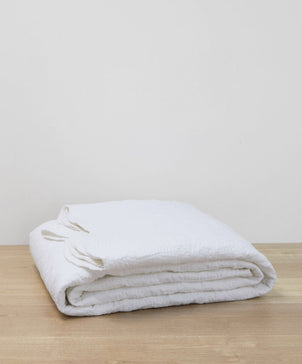 Folded white blanket on a wooden surface with a light gray background