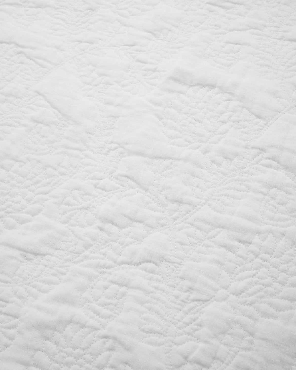 White quilted fabric with a subtle, intricate stitched pattern. The texture and stitching create a gentle, soft appearance.