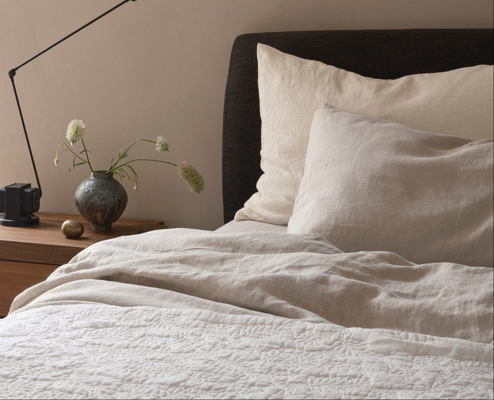 Neatly made bed with white bedding and pillows, nightstand with decorative items.