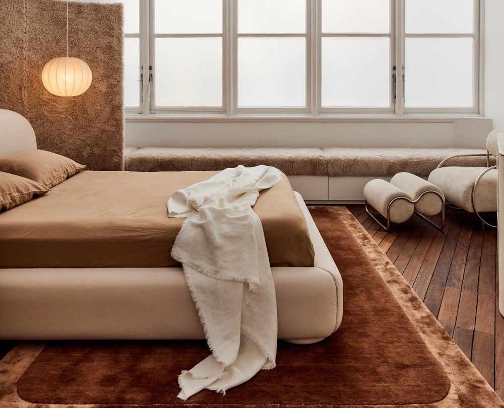 Neatly made bed with white bedding and pillows, nightstand with decorative items.