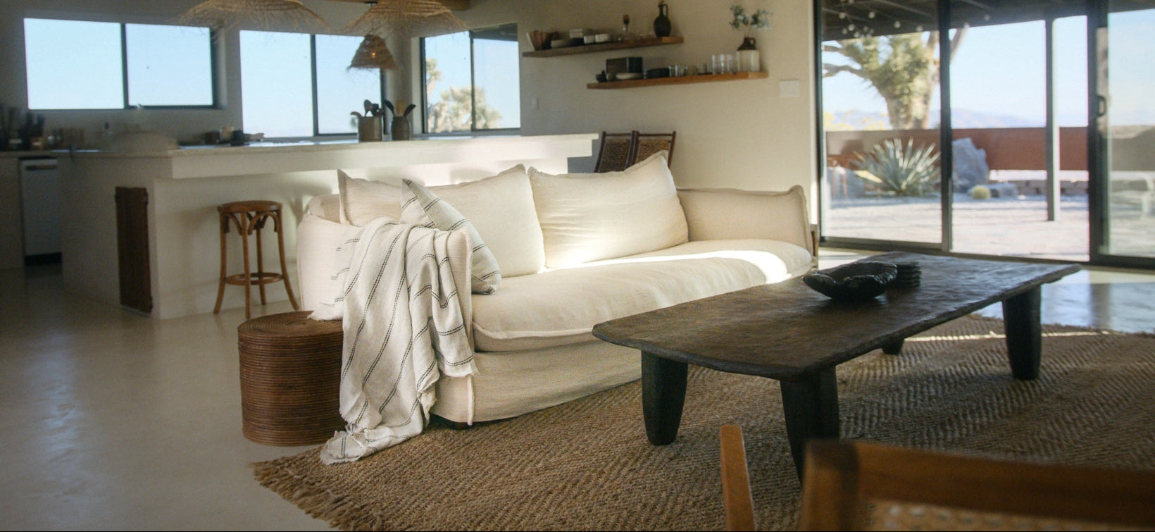 Modern living room with a white sofa, wooden coffee table, and large windows.