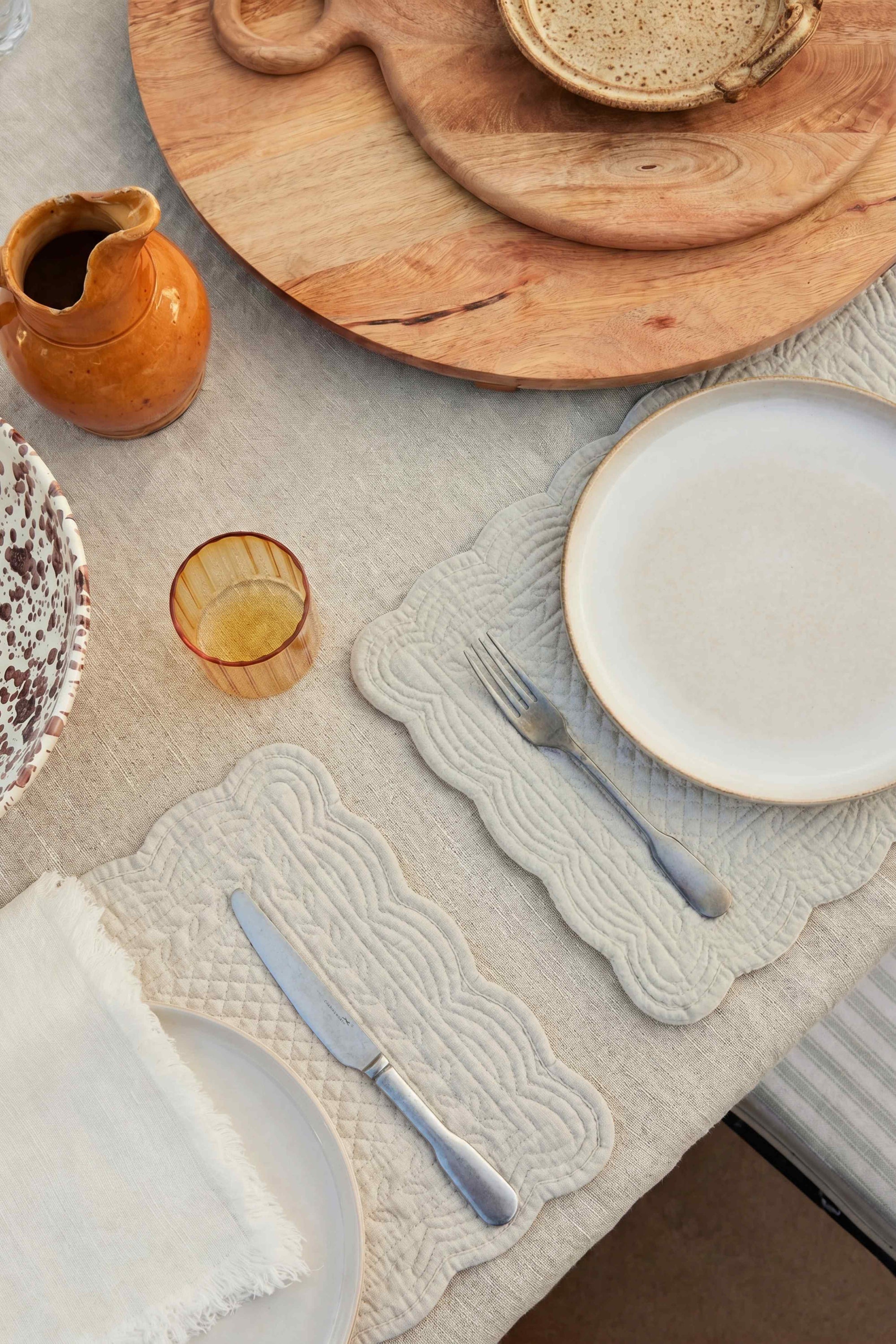 table with beige placemats on it with cutlery.