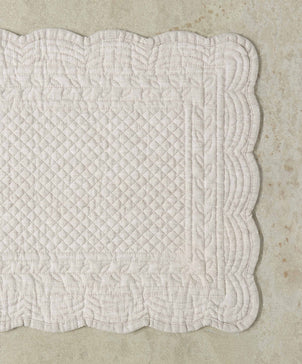 Quilted white fabric with a scalloped edge on a beige background