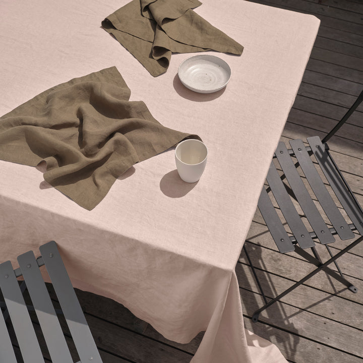 An outdoor table setting featuring a Linen Tablecloth in Blush, paired with Linen Napkins in Olive