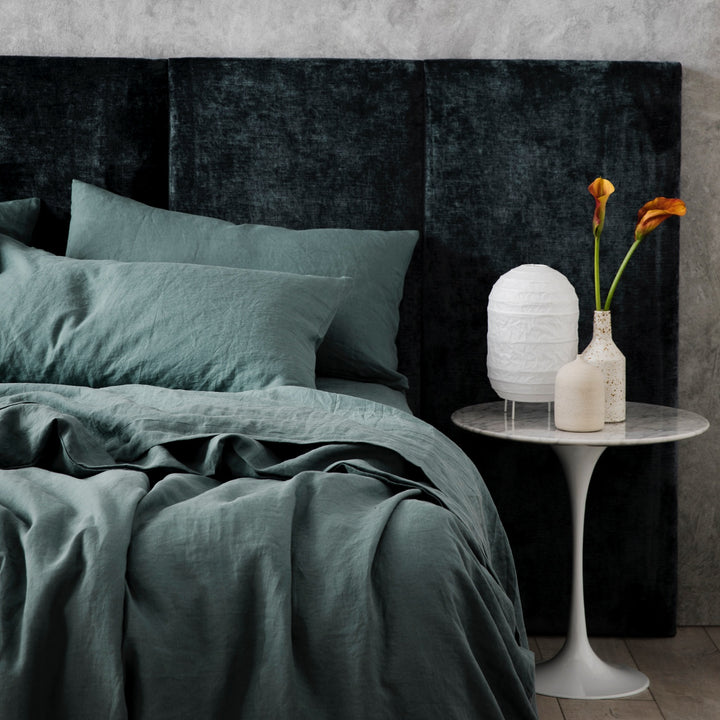 A bed dressed in Bluestone bed linen, styled with a velvet headboard, modern bedside table, small ceramic vases and small white lantern. Sizes: Queen, King