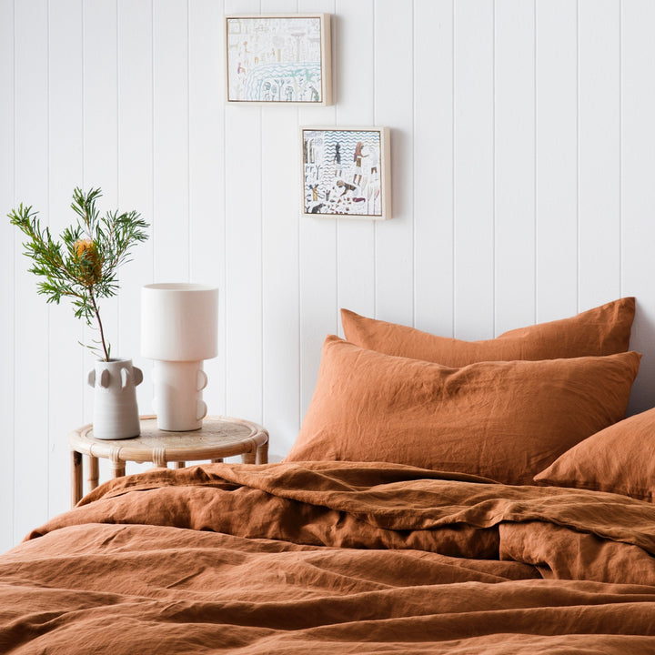 A bed dressed in Cedar Stripe bed linen, styled with a bamboo bedside table and ceramics
