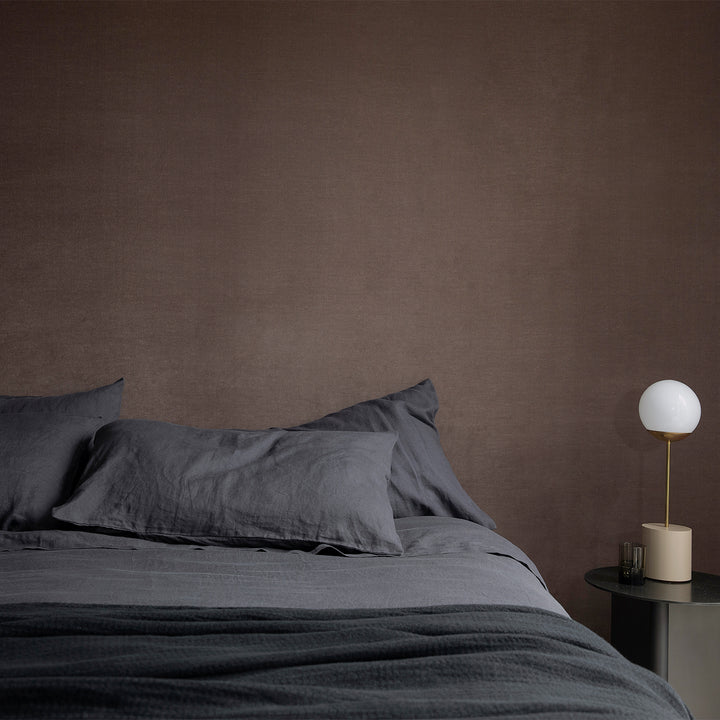 A bed dressed in Slate bed linen, styled with a modern bedside table and lamp
