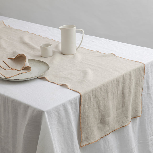 Cara Edged Table Runner in Natural on a Linen Tablecloth in White