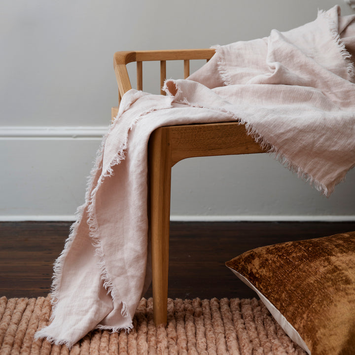 A wooden bench seat styled with a Freya Linen Throw and Talik Cushion in Fawn