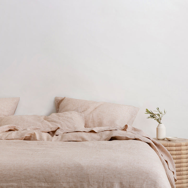 A bed dressed in Cinnamon bedlinen, styled with a side table and small vase.